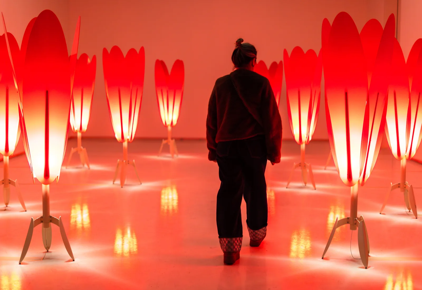 A lone visitor walking through the field of glowing red tulip lamps