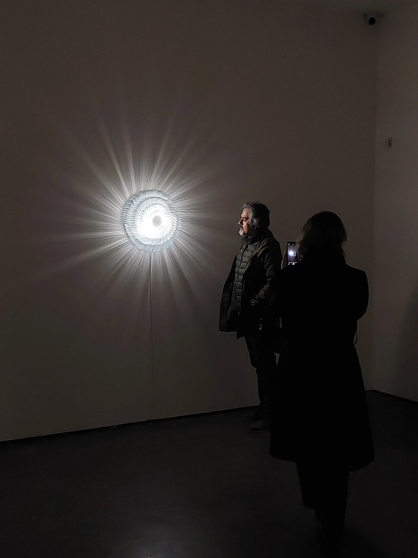 Visitors in the darkened IranShahr Gallery, lit by a radial light work