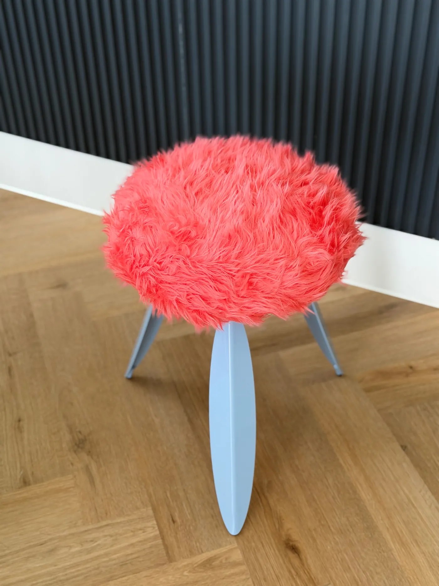 The fur stool on a herringbone oak floor against a dark slatted wall
