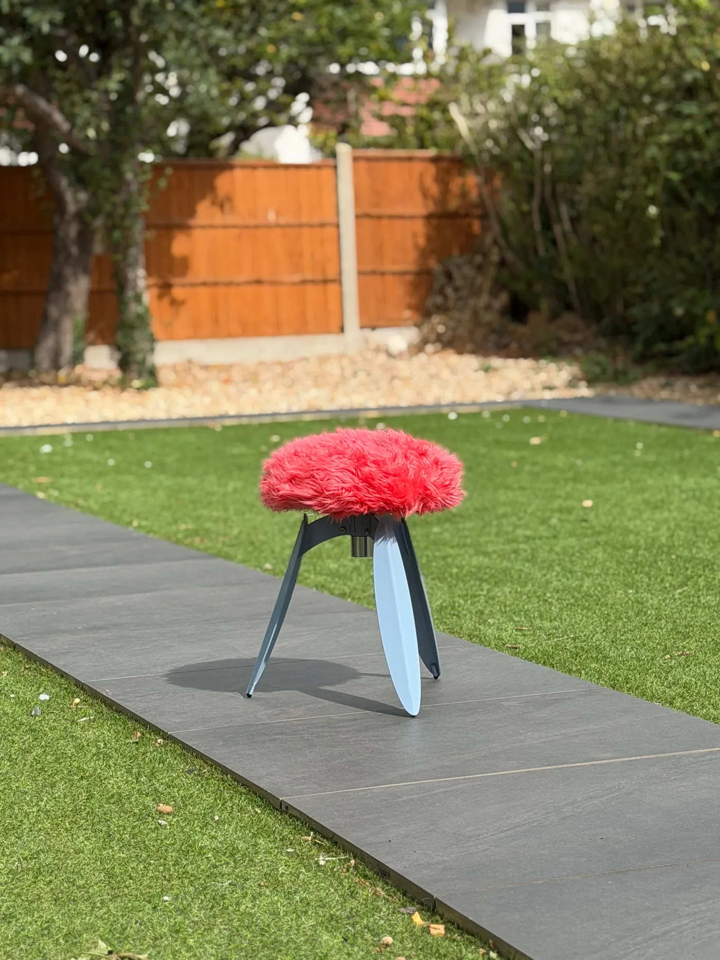 The fur stool outside, on the paving beside a lawn