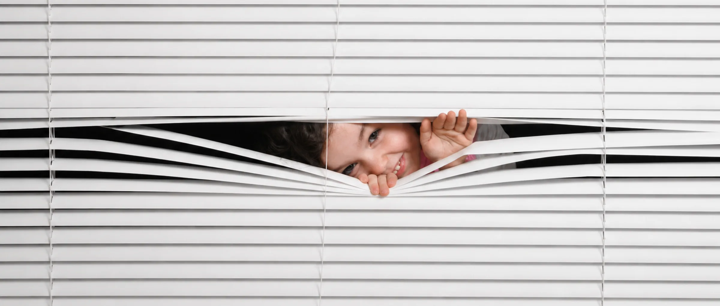 A child peeking through white venetian blinds — the material Keker is born from